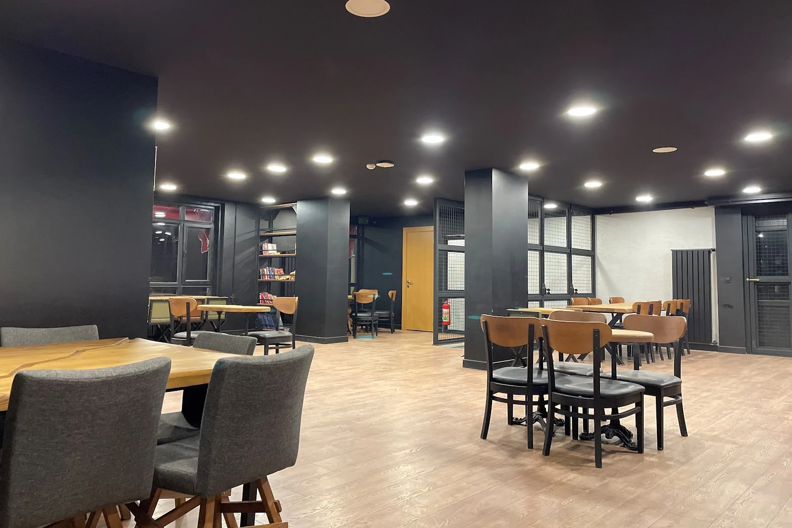 Arabica Coffee House Emek şubesinin geniş iç salonu: ahşap masalar, gri ve hardal renkli sandalyeler, siyah tavan ve spot ışıklar