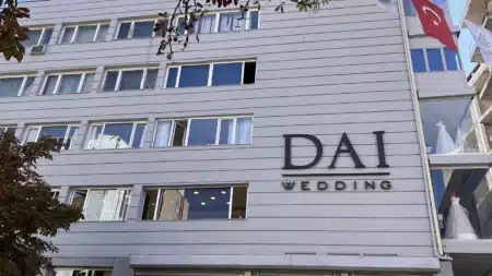 Ankara’nın En İyi Gelinlikçileri ve Gelinlikçiler Çarşısı (Güncel Liste) Tunalı Hilmi Caddesi’ndeki Dai Wedding binası: gri yatay kaplamalı çok katlı cephede “DAI WEDDING” harfleri, sağda Türk bayrağı ve camlı vitrinde gelinlikler, solda kestane ağacı dalları