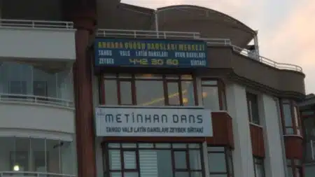 Ankara Dans Kursları ve Dans Okulları (Güncel Liste) Apartman cephesinde lacivert zeminli “Ankara Düğün Dansları Merkezi” tabelası (tango, vals, Latin dansları, oyun havaları, zeybek, sirtaki ve 442 30 60 telefonu), altında beyaz “Metinhan Dans” tabelası; kahverengi doğramalı pencereler ve çatı katında gergi tente