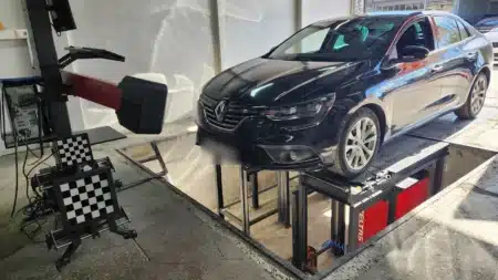 Rot ayarı çukurunun üstünde siyah bir Renault Megane; solda kameralı 3B rot ayarı cihazı ve satranç tahtası desenli tekerlek hedefleri