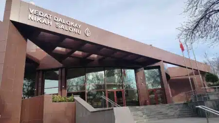 Kırmızı granit kaplı Vedat Dalokay Nikah Salonu binasının girişi: cephede “VEDAT DALOKAY NİKAH SALONU” yazısı ve Çankaya Belediyesi yaprak amblemi, camlı giriş kapıları, merdivenler ve bayrak direkleri