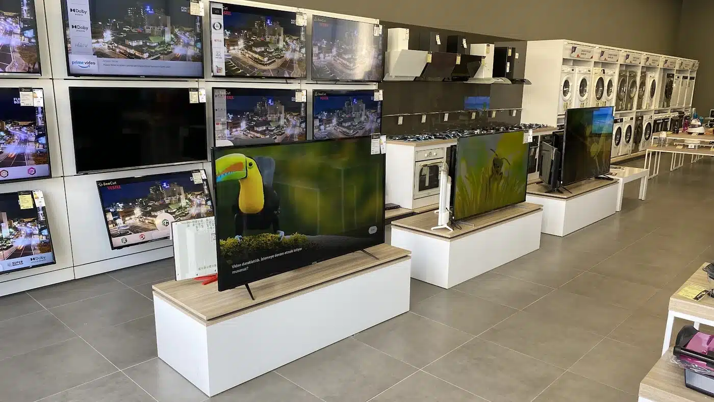 Vs Outlet Ankara mağazasının içi: solda duvara asılı ve önde ahşap tablalı beyaz sehpalarda sergilenen Vestel televizyonlar, ortada ankastre fırın, ocak ve davlumbazlar, sağda raflara dizili çamaşır ve kurutma makineleri