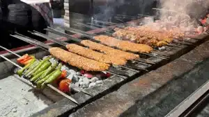 Zırhçı Kebap’ta kömür ateşi üzerinde şişlerde pişen Adana kebaplar, yanlarında sivri biber ve domates şişleri